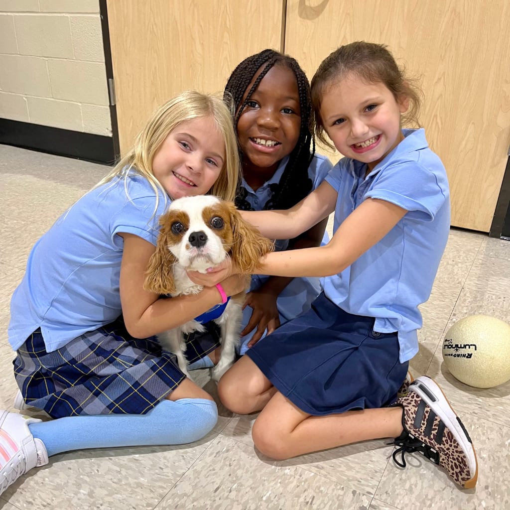 There Briarwood students smile as they hold and pet a dog.