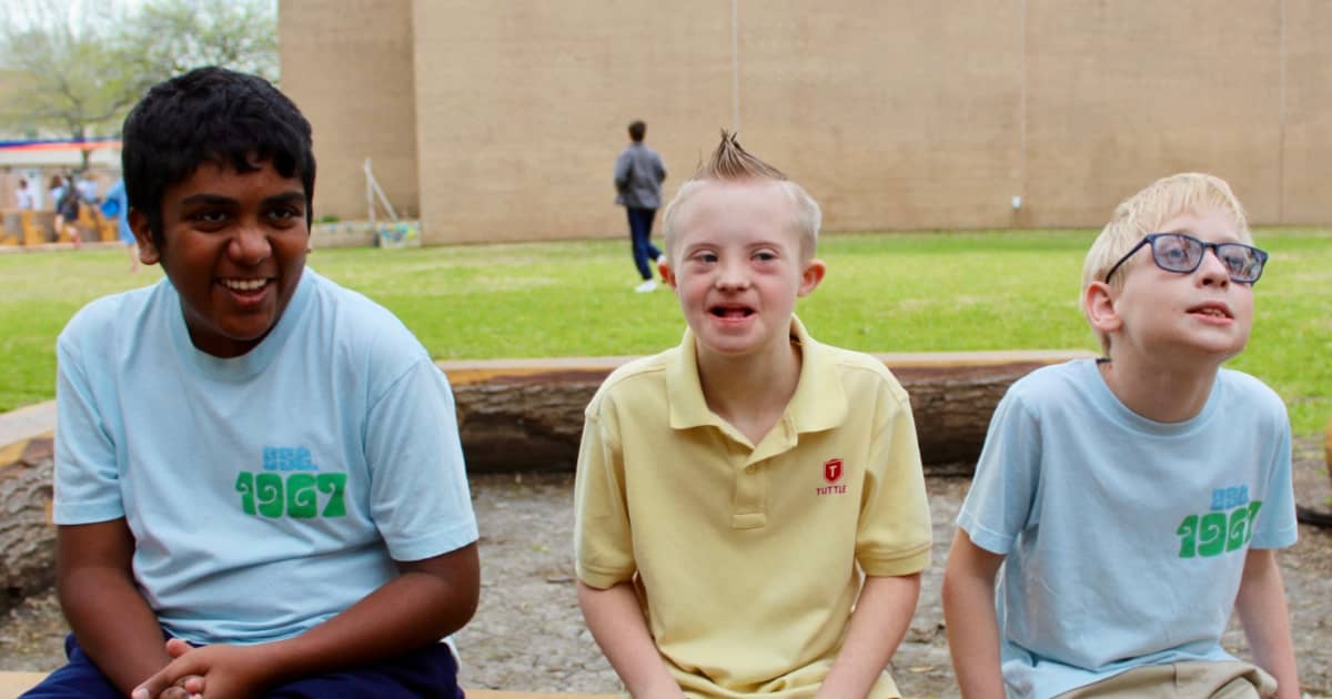 Three Tuttle elementary students sit on a log and smile.