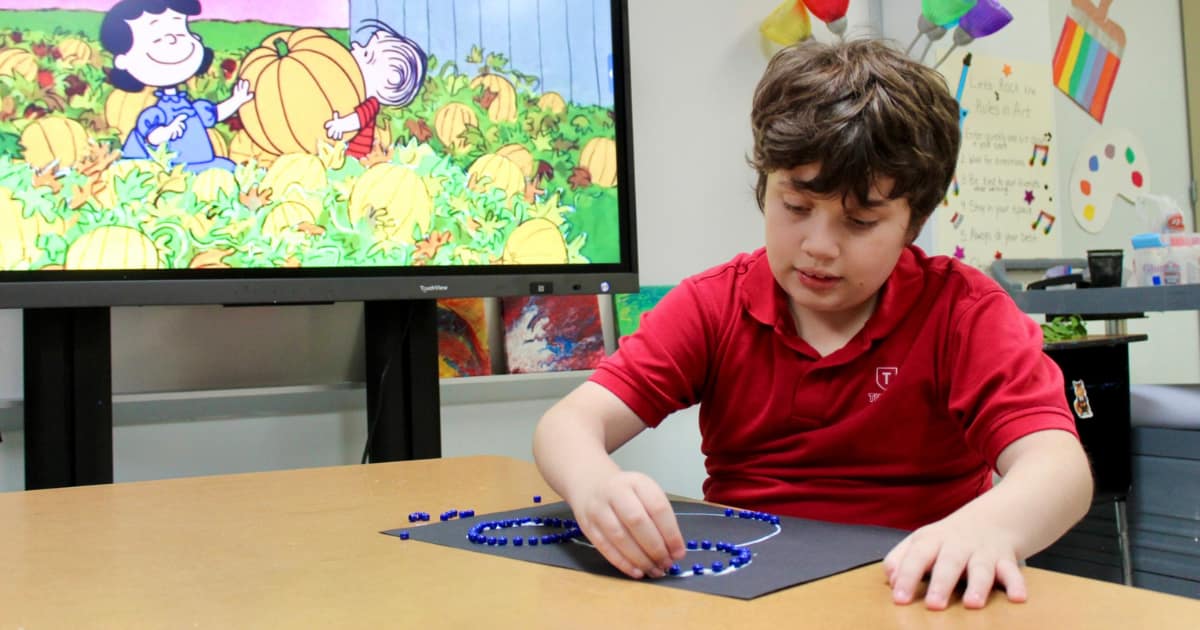 Tuttle elementary student places colored beads in the shape of Mickey Mouse on a paper.