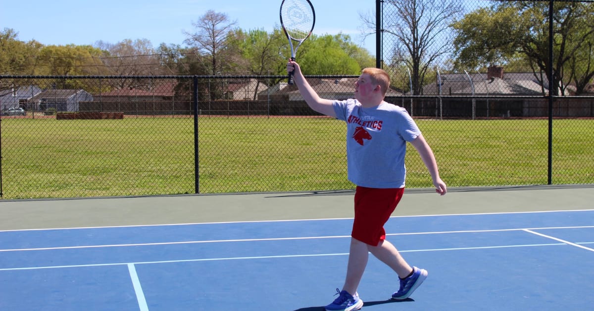 Tuttle middle school student smiles as he hits a tennis ball with a racket.