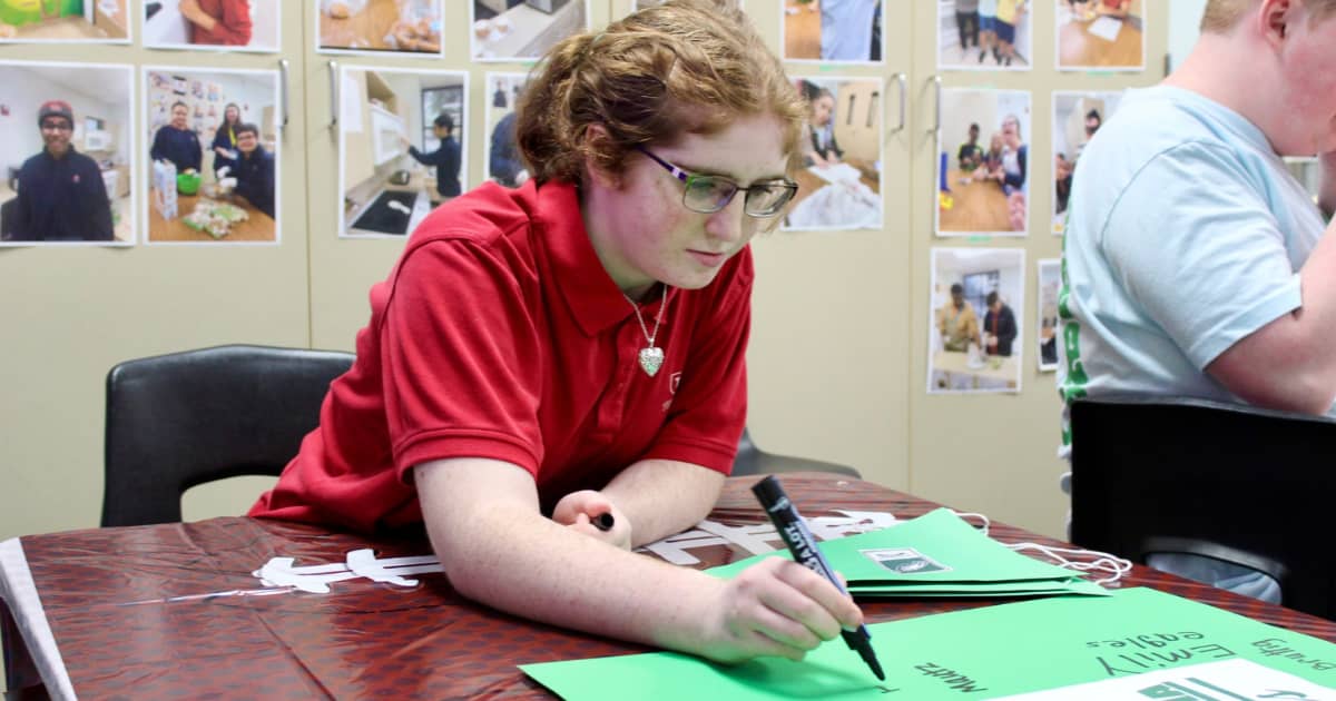 Tuttle student uses a sharpie to draw on green paper.