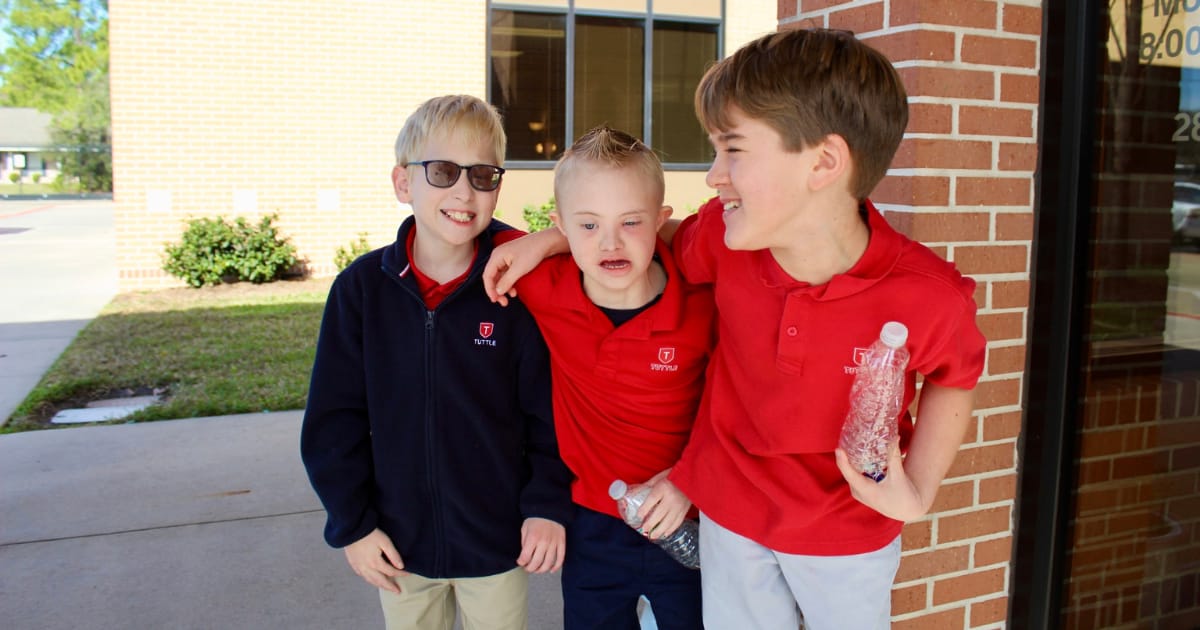 Three Tuttle students stand with each other and smile while outside of a building.