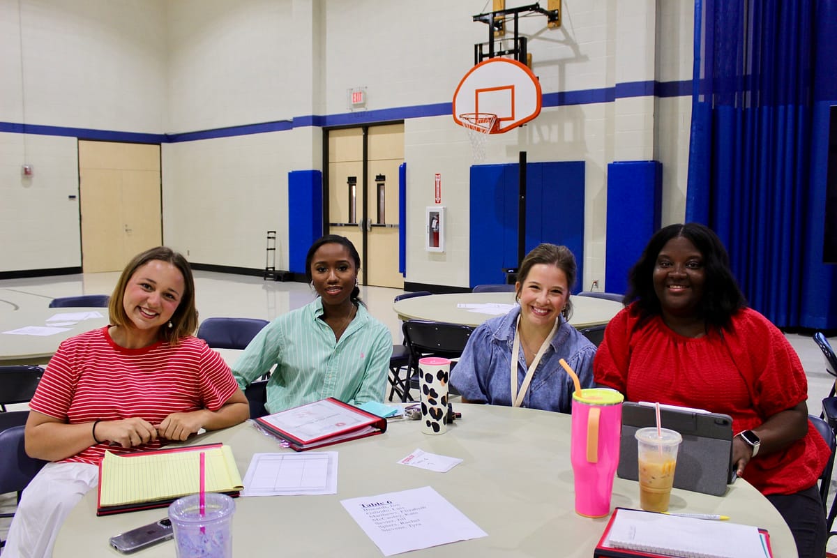 Four teachers sit at a table and smile at the camera.