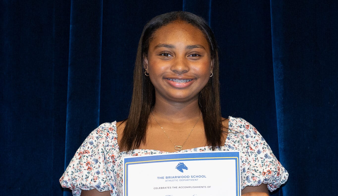 Briarwood middle school student holds a paper certificate and smiles.