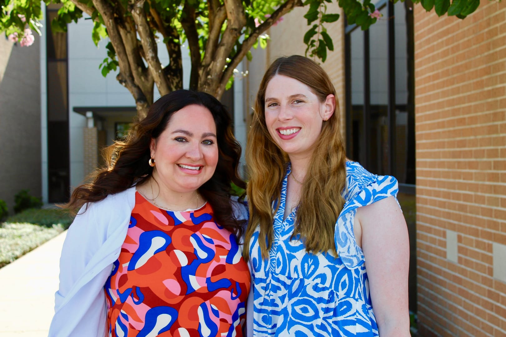 Mallary and Ashley stand together and smile in front of a tree.