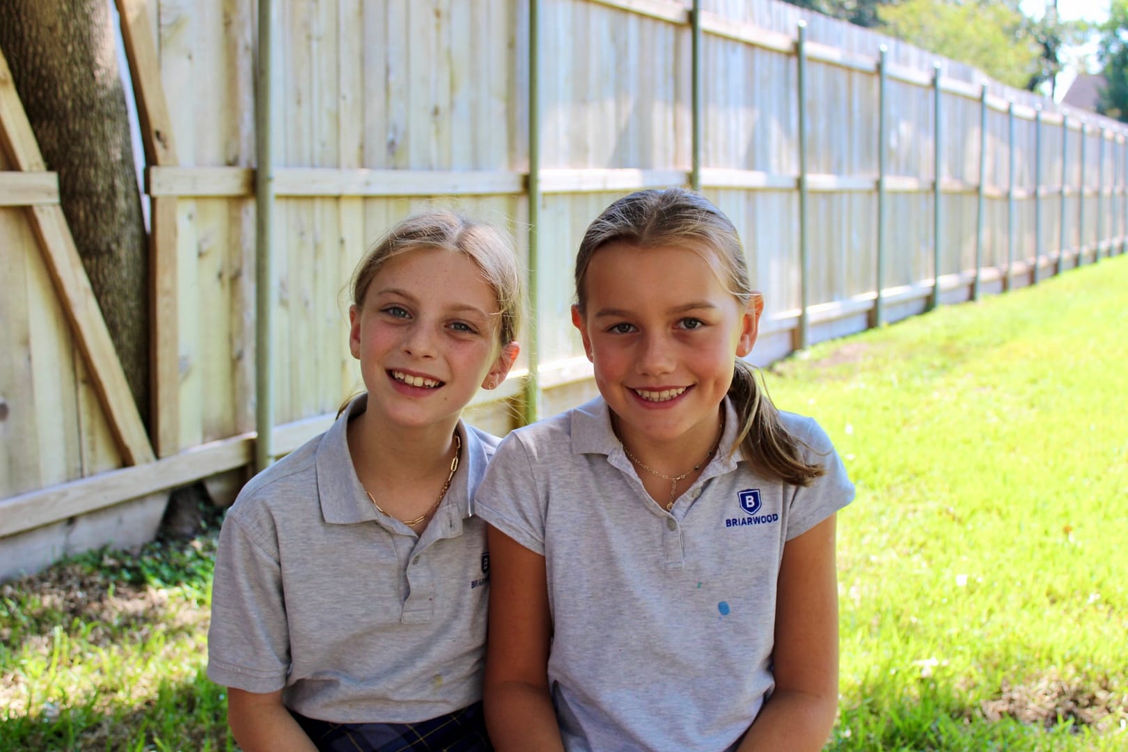 Two girls sit outside and smile.