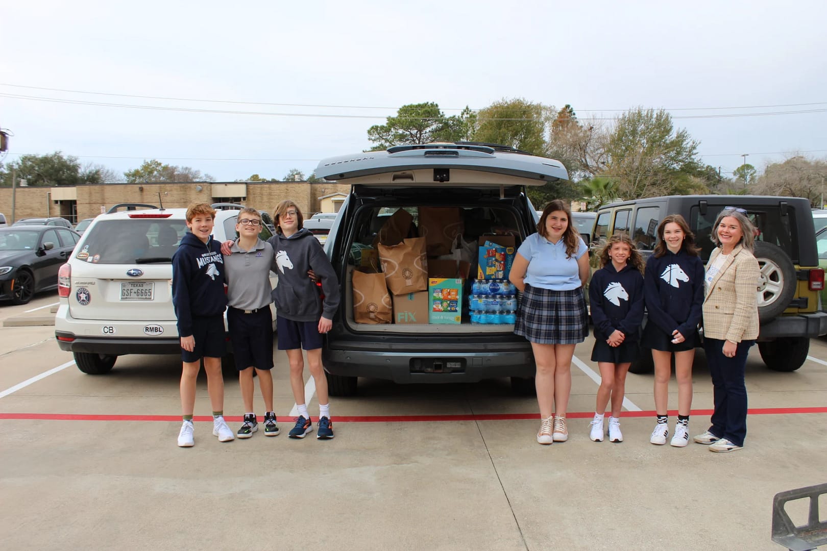 Middle schoolers and adults stand in front of a packed car trunk with food packs.