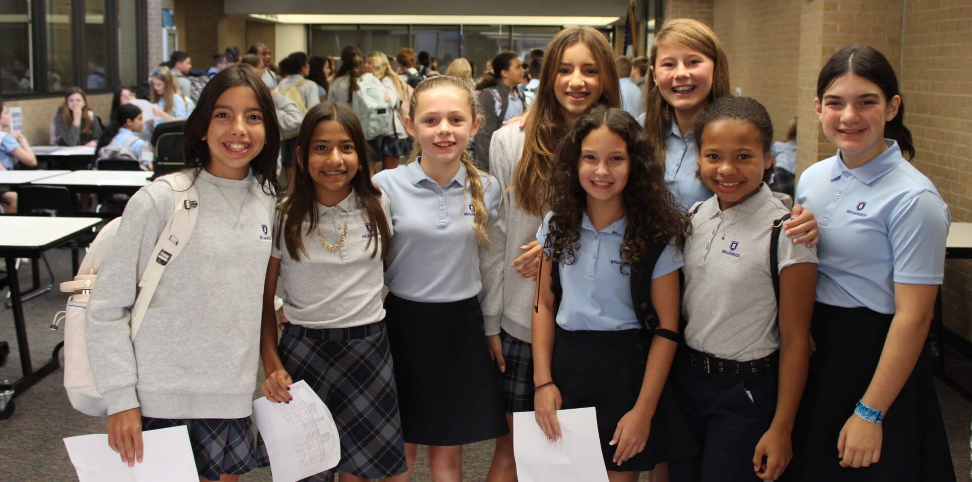 Six students stand together in the lunch room and smile, looking at the camera.